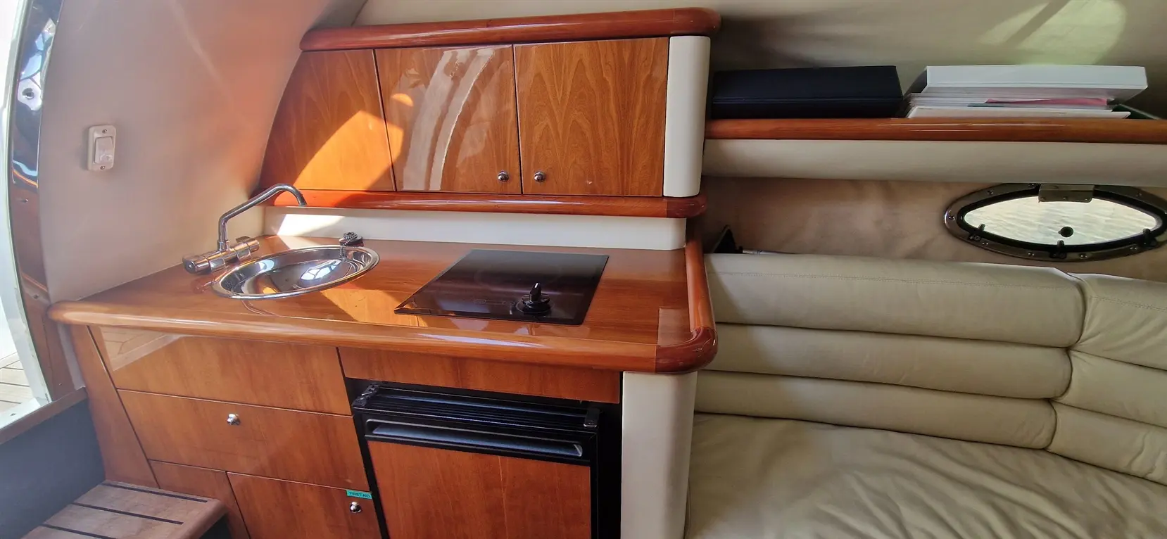 Modern boat kitchenette features a sink, induction cooktop, and storage cabinets, with a cozy leather sofa nearby.